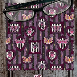 May include: Purple and black striped fabric with a repeating pattern of framed butterflies, beetles, and scorpions. The fabric is designed for cleaning glasses.