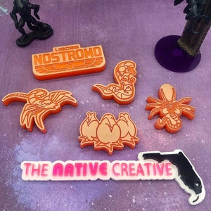 May include: Orange and white plastic figurines of an alien, a facehugger, a chestburster, and a xenomorph. The figurines are on a purple background with a white background with the text "THE NATIVE CREATIVE" and a black outline of the state of Florida.