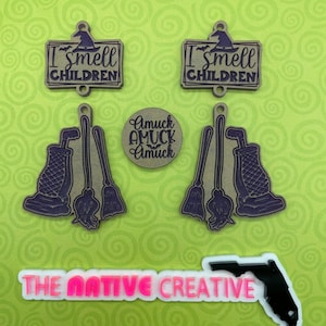 May include: A collection of laser-cut wooden Halloween-themed charms and a sticker. The charms include two signs that read "I smell children" with a witch hat, two sets of a vacuum cleaner and brooms, and a round charm with "Amuck Amuck Amuck". The sticker says "The Native Creative" with a Florida outline.