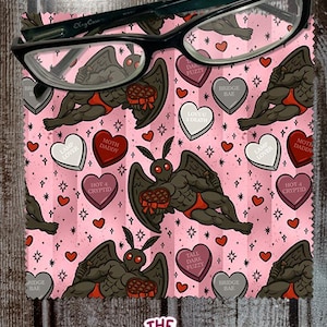 May include: A pair of black-framed eyeglasses rests on a pink cleaning cloth. The cloth features a repeating pattern of a moth-like creature, hearts, and text. The text includes phrases like "Moth Daddy" and "Tall Dark Fuzzy". The Native Creative logo is at the bottom.