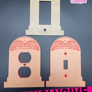 May include: A set of decorative wall plates in a unique design. The set includes a light switch cover, an outlet cover, and a switch cover. Each plate features a detailed design with a face and wings. The text "EXCLUSIVE WALL PLATES" is visible.