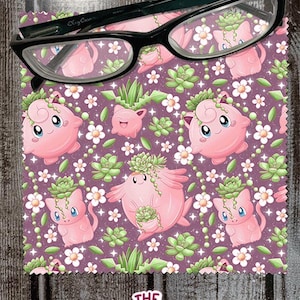 May include: A microfiber cleaning cloth with a purple background featuring pink cartoon characters with succulent plant accents and white flowers. Black framed eyeglasses rest on top. The Native Creative logo is in the bottom right corner.