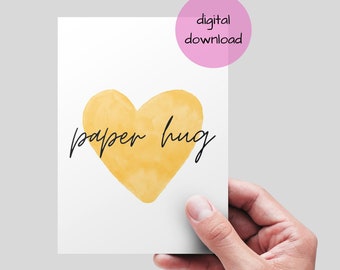 May include: A white card with a watercolor-style yellow heart and the words "paper hug" in black script. A pink circle with the words "digital download" is in the upper right corner. The card is held by a hand.