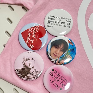 May include: A collection of five round pinback buttons. One button has the text "Heart on the Window" with a red heart. Another has a photo of a person. The remaining buttons have text in English and Korean.