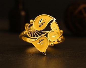 May include: A gold ring featuring a leaf design. The ring has three main leaves with etched details and small, round accents. The ring is set against a dark background, highlighting its bright, polished finish.