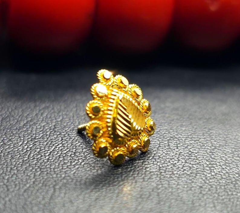 May include: A gold nose ring with a heart-shaped design and intricate detailing. The ring is made of a delicate metal and has a polished finish.