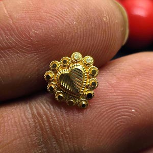 May include: A gold nose ring with a heart-shaped design and a circle of small stones around the edge.