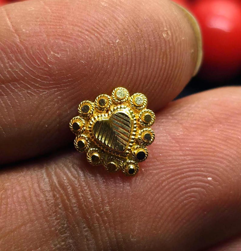 May include: A gold nose ring with a heart-shaped design and a circle of small stones around the edge.