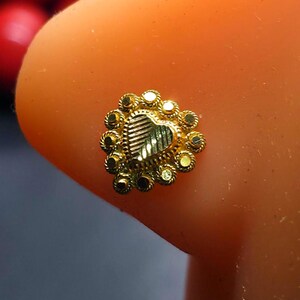 May include: A gold nose ring with a heart-shaped design and a circle of small gold beads around the edge.
