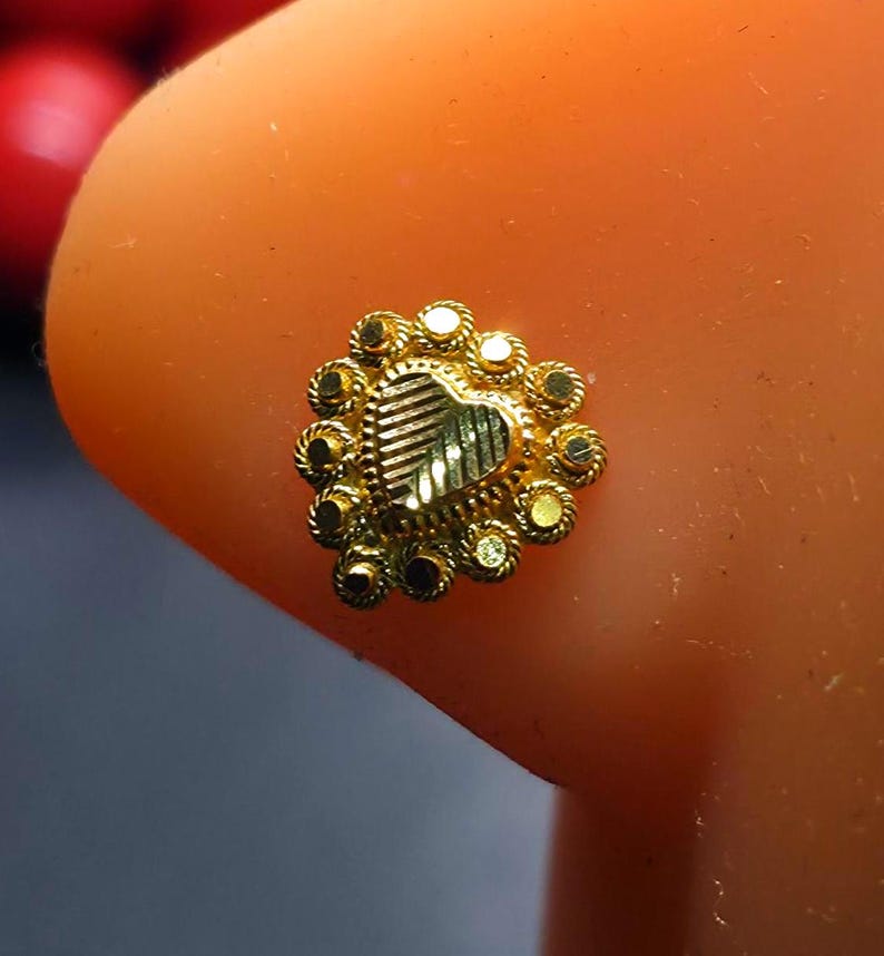 May include: A gold nose ring with a heart-shaped design and a circle of small gold beads around the edge.