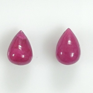 May include: Two teardrop-shaped pink gemstones, likely rubies, are shown on a white background.