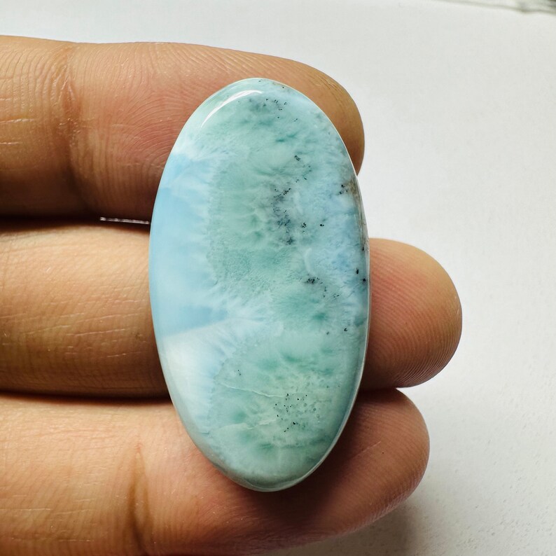May include: A light blue oval cabochon gemstone with a cloudy, marbled pattern and black flecks.