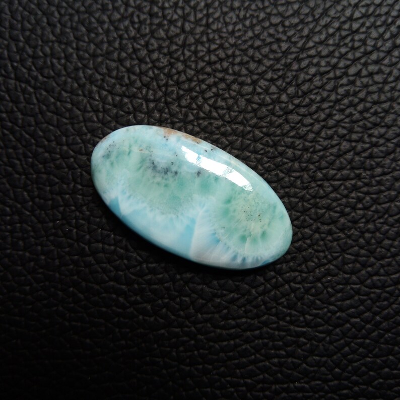 May include: A light blue, oval-shaped cabochon gemstone with white and green swirls and brown flecks.