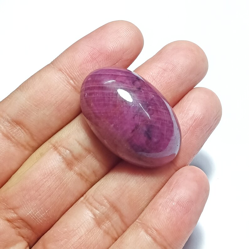 May include: A large, oval-shaped, cabochon cut, pink ruby gemstone with a polished, glossy finish.