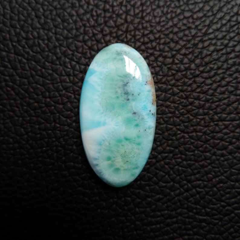 May include: A light blue, oval-shaped cabochon gemstone with white and green swirls and dark flecks.