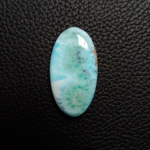 May include: A light blue, green, and white oval cabochon gemstone with a cloudy, marbled pattern. The gemstone has a smooth, polished surface.