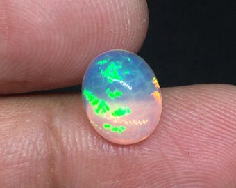 Puede incluir: Una piedra preciosa de ópalo en cabujón de forma ovalada con una base blanca translúcida y destellos vibrantes de color verde neón y sutiles tonos naranja. La piedra tiene una superficie lisa y pulida que refleja la luz con claridad.
