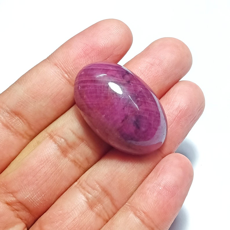 May include: A large, oval-shaped, cabochon cut, pink ruby gemstone. The ruby has a smooth, polished surface and a deep, rich pink colour.