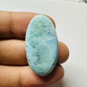 May include: A light blue oval cabochon gemstone with a cloudy, marbled pattern. The stone has a smooth, polished surface.