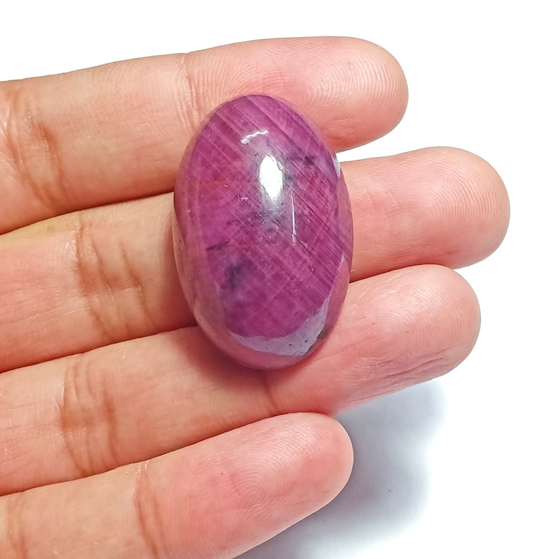 May include: A large, oval-shaped, pink gemstone with a smooth, polished surface. The gemstone has a deep, rich pink colour and is set in a silver ring.