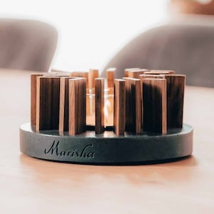 Peut inclure: Un bougeoir en béton gris avec un cadre en bois et une bougie en verre au centre. Le bougeoir est inscrit du nom "Marisha".