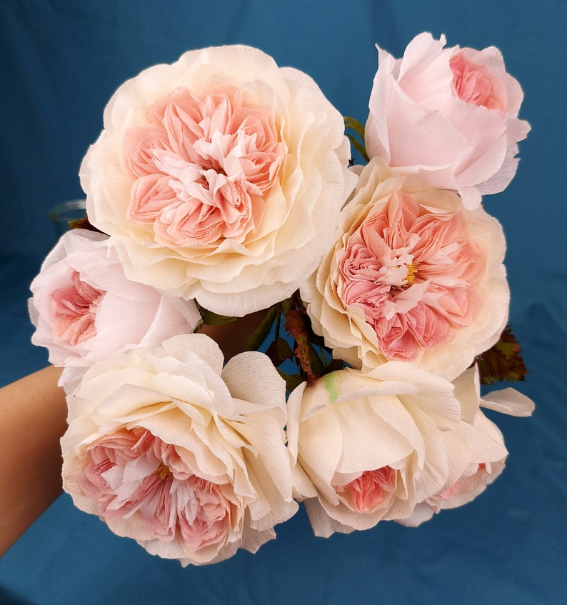 May include: A bouquet of six delicate, paper roses in shades of pink and white. The roses are arranged in a cluster, with the stems hidden from view.