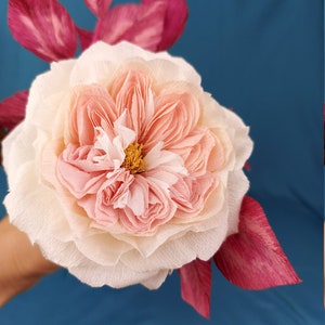 May include: A delicate paper flower with a pink and white center and pink petals. The flower is surrounded by pink leaves.