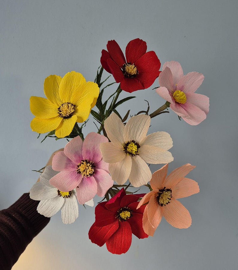 May include: A bouquet of paper flowers in various colors, including red, yellow, pink, and white. The flowers are arranged in a cluster and have a delicate, layered appearance.