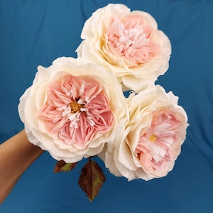 May include: Three delicate paper roses in shades of pink and white. The roses are arranged in a bouquet and have a realistic appearance.