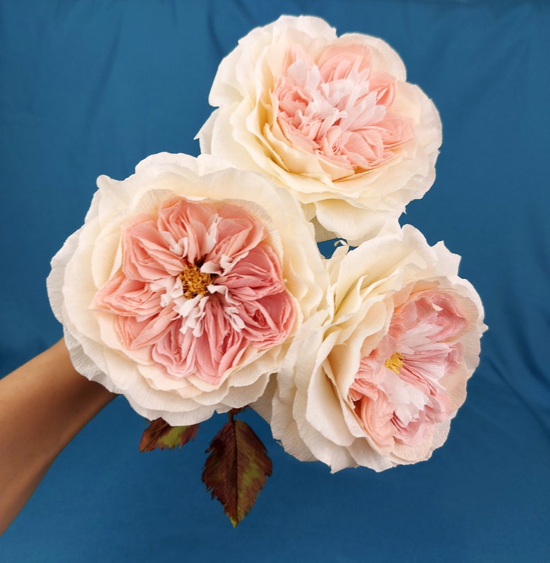 May include: Three delicate paper roses in shades of pink and white. The roses are arranged in a bouquet and have a realistic appearance.