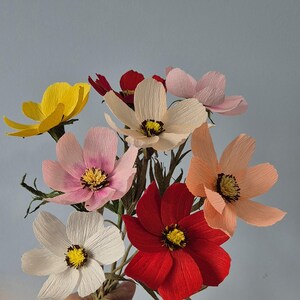 May include: A bouquet of paper flowers in various colors, including yellow, pink, white, red, and peach. The flowers are made of crinkled paper and have a realistic appearance.