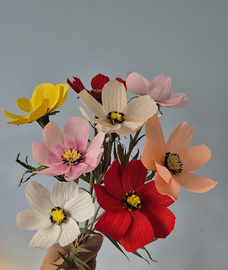 May include: A bouquet of paper flowers in various colors, including yellow, pink, white, red, and peach. The flowers are made of crinkled paper and have a realistic appearance.