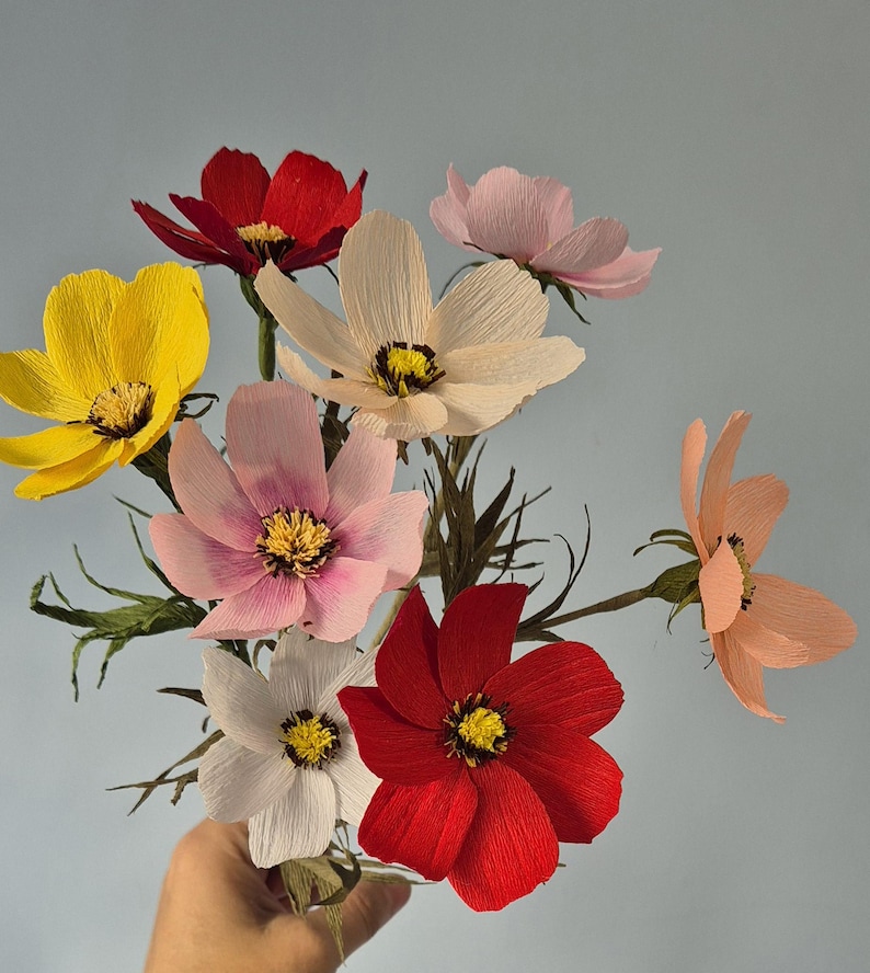 May include: A bouquet of paper flowers in various colors, including red, pink, yellow, and white. The flowers are arranged in a hand-held bouquet.