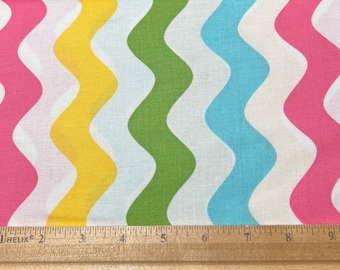 May include: Fabric featuring a repeating wavy pattern in pink, yellow, green, and blue on a white background. A wooden ruler is at the bottom, measuring in inches.