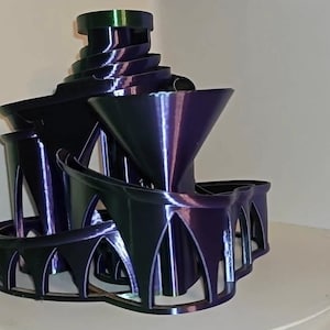 Könnte beinhalten: Eine 3D-gedruckte Skulptur aus mehreren übereinander gestapelten Trichtern und Bögen. Die Skulptur ist aus dunkelviolettem und grünem, irisierendem Kunststoff.