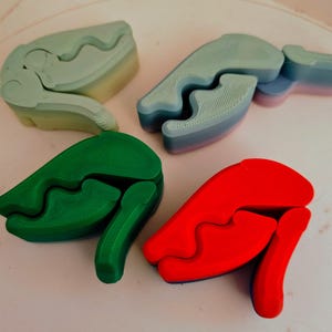 Può includere: Quattro oggetti astratti stampati in 3D dai colori vivaci. Gli oggetti sono in tonalità di verde, blu e rosso. Ogni oggetto ha una forma unica con elementi curvi e angolari. Gli oggetti sono disposti su una superficie chiara.