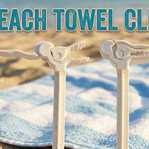 Op de afbeelding: Twee crèmekleurige strandlakenclips met een getextureerde afwerking, ontworpen om handdoeken vast te zetten. De clips staan op een blauw-wit gestreepte handdoek, met de woorden "BEACH TOWEL CLIP" in turquoise.