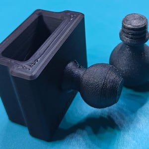 Könnte beinhalten: Eine schwarze, 3D-gedruckte rechteckige Komponente mit hohler Mitte und einem an einer Seite befestigten Kugelgelenk, begleitet von einem separaten schwarzen Kugelgelenkteil mit einer Gewindeschraube zur Montage und Verbindung.
