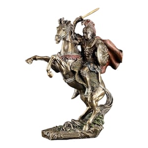 May include: A bronze-toned statue of a warrior in ancient armor riding a rearing horse. The figure wears a crested helmet and a flowing red cape, holding a sword aloft and a round shield. The base features the text "ALEXANDER THE GREAT".