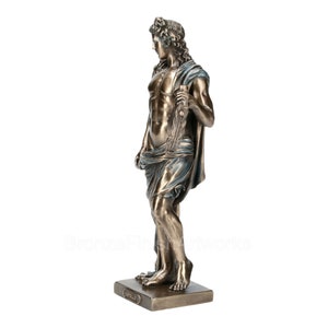 Puede incluir: Una estatua de color bronce de Apolo de pie sobre una base rectangular. La figura tiene el pelo largo y ondulado, una complexi&oacute;n musculosa y est&aacute; envuelta en una tela con tonos azules. El nombre Apolo est&aacute; inscrito en una placa.