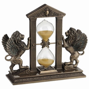 May include: A bronze hourglass with winged lion statues on each side, set within a decorative columned frame. The hourglass has a clear glass bulb and gold sand.