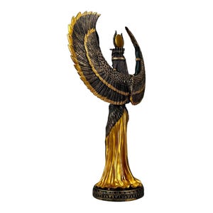 May include: A gold and black statue of the Egyptian goddess Isis with outstretched wings. The statue is standing on a base with intricate details.