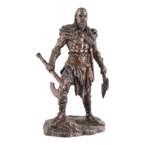 May include: A bronze-effect statue of a Viking warrior, holding two axes. The figure has a long beard and is wearing detailed armour and clothing. The statue is mounted on a rocky base, with intricate detailing throughout the design.