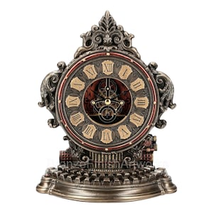 May include: A bronze clock with a Roman numeral clock face and intricate details. The clock is set on a base that resembles a typewriter.