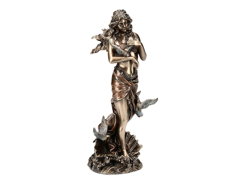 May include: A bronze sculpture of a woman standing on a wave with birds flying around her. She is holding a seashell in her hand. The sculpture is painted in shades of brown and blue.