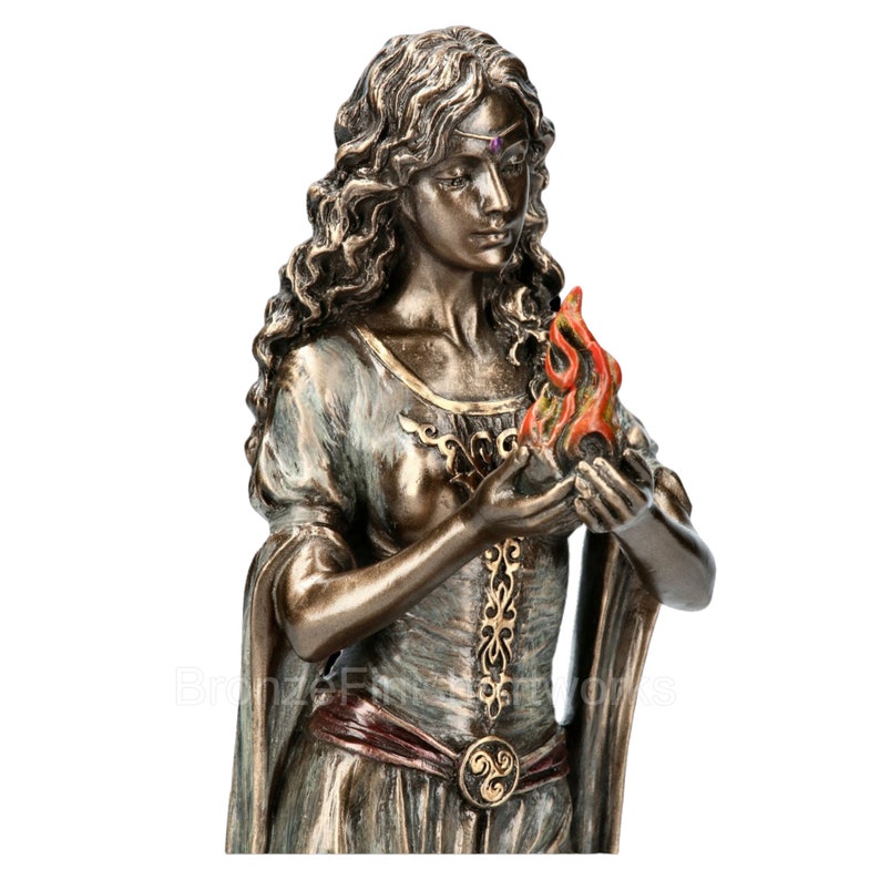 Puede incluir: Escultura de bronce de una mujer con el pelo largo y suelto que sostiene una llama en sus manos. Lleva un vestido largo y fluido con una faja roja y un cintur&oacute;n dorado. La escultura es detallada e intrincada.