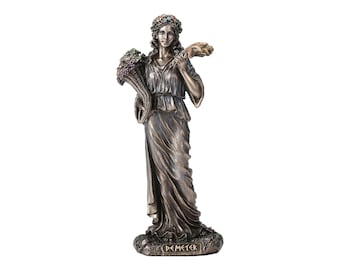 Può includere: Statua in bronzo della dea greca Demetra, che tiene una cornucopia piena di fiori e una spiga di grano. La statua è in piedi su una base con la scritta "Demetra" incisa su di essa.