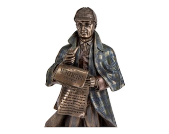 May include: A bronze-toned figurine of a detective wearing a plaid deerstalker hat and a matching plaid cape. The figure holds a pipe in one hand and a newspaper with the text "SHASTLY MURDER IN THE EAST-END" printed on the front page.