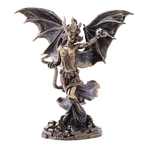 Könnte beinhalten: Bronzefarbene Statue von Lilith, einer mythologischen Figur, mit großen fledermausartigen Flügeln. Sie trägt eine Krone und einen Rock und hält einen Schädel und eine Schlange. Die Statue steht auf einem Sockel mit Schädeln und dem Namen "LILITH".
