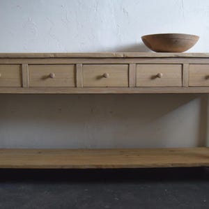 May include: A light wood console table with four drawers and a lower shelf. The table has a simple, rustic design and is made of natural wood.